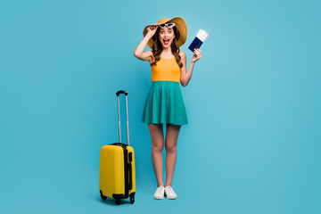 Full body photo of pretty lady traveler hold passport tickets rolling suitcase luggage airport cheap flights wear sun specs short summer dress headwear shoes isolated blue background