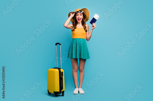 Full body photo of pretty lady traveler hold passport tickets rolling suitcase luggage airport cheap flights wear sun specs short summer dress headwear shoes isolated blue background