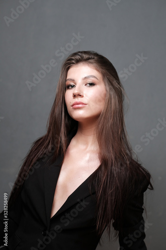 Close-up portrait of a beautiful cute girl with long hair and in a black jacket on a light background. Girl posing for the photographer in a photo studio.