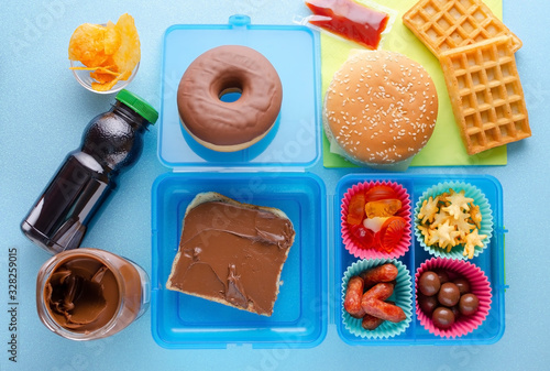 Lunch box with unhealthy food on blue background, top view