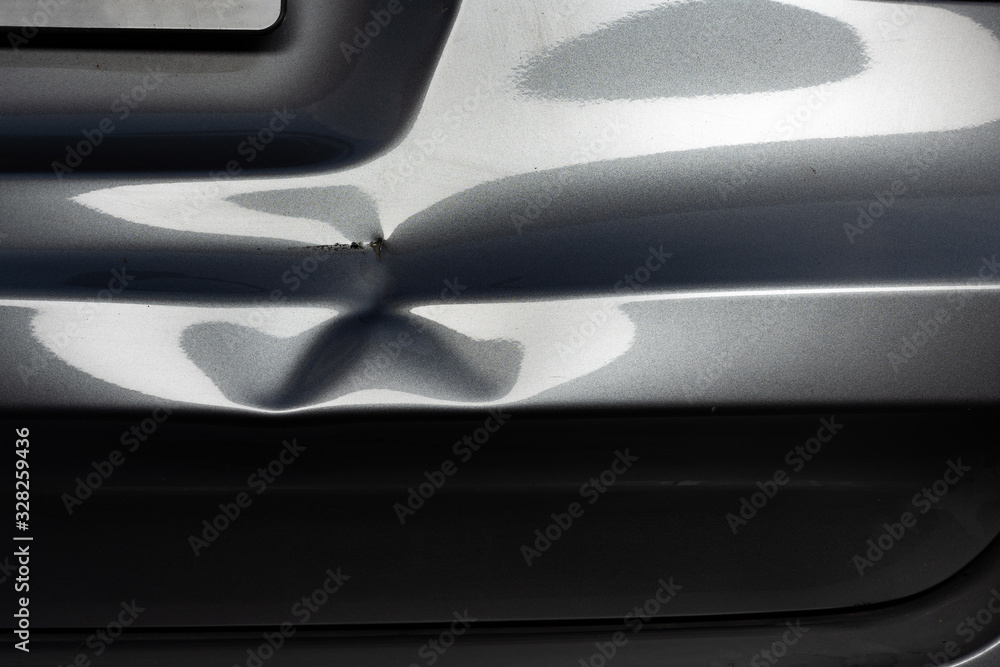 A dent in a metal fold of a silver car in exciting light.