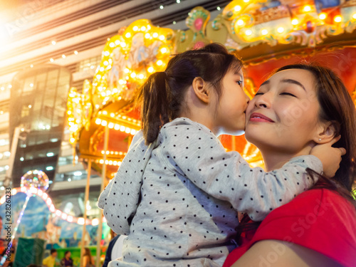 happy asia mother and daughter have fun in amusement carnival park with farris wheel and carousel background photo