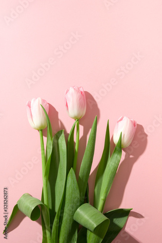 Bouquet of pink tulips with sunny shadow on pastel pink. Top view. Happy holiday. Greeting card for Mother day or romantic anniversary. Vertical format.