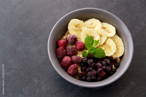 food and breakfast concept - oatmeal cereals in bowl with wild berries, banana and peppermint on slate stone table