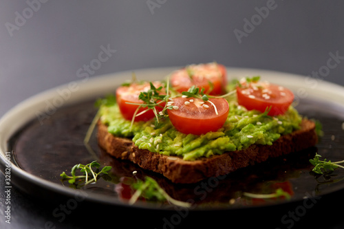 food, eating and breakfast concept - toast bread with mashed avocado, cherry tomatoes and greens on ceramic plate