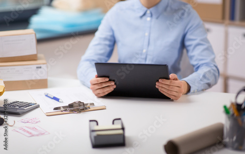 delivery, mail service, people and shipment concept -woman with tablet pc computer, parcel boxes and form on clipboard at post office