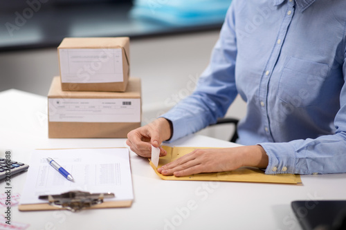 delivery, mail service, people and shipment concept - close up of woman's hands removing sticker from envelope with parcel at post office