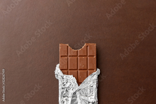 sweets, confectionery and food concept - milk chocolate bar in foil wrapper on brown background