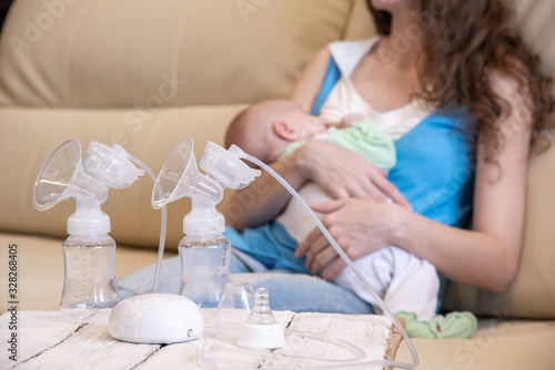 A young mother breastfeeds her baby and an electric breast pump is standing in front of her on a table