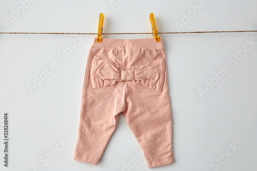 clothes, laundry, babyhood and clothing concept - pink pants for baby girl with bow hanging on clothesline with pins on white background photo