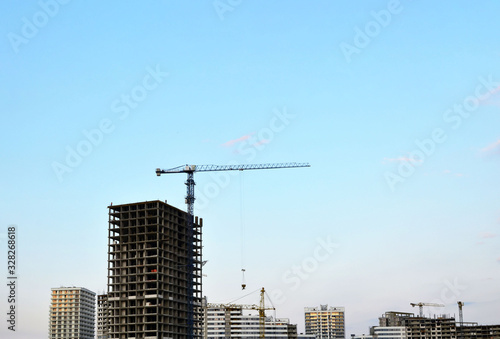 Tower crane and new residential high-rise buildings at a huge construction site on sunset background. Building construction, installation of formwork and concrete structures