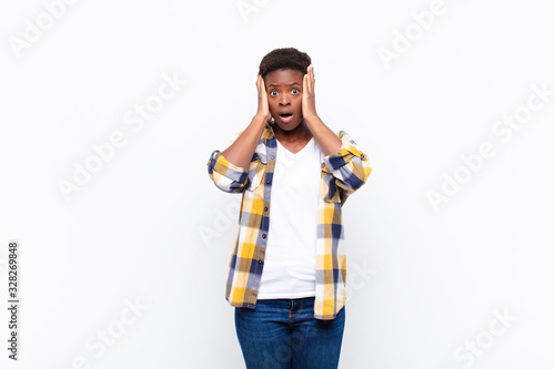 young pretty black womanlooking unpleasantly shocked, scared or worried, mouth wide open and covering both ears with hands photo