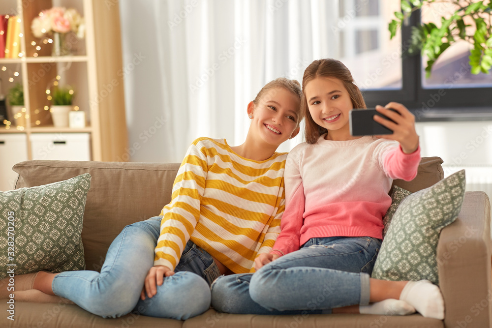 people, technology and friendship concept - happy teenage girls taking selfie with smartphone sitting on sofa at home