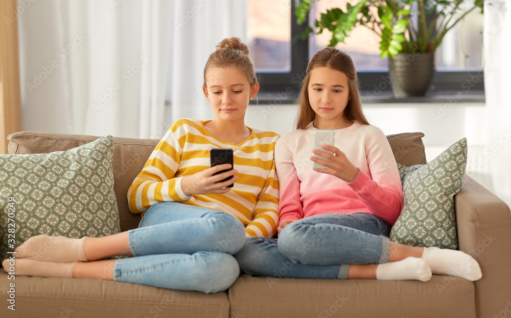 people, technology and friendship concept - teenage girls with smartphones sitting on sofa at home
