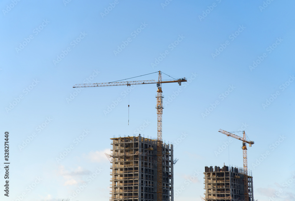 Tower cranes working at construction site against blue sky. Crane lifting a concrete bucket. Construction process of the new residential buildings. Transportation blocks and pouring of the cement mix Tower cranes working at construction site against blue sky. Crane lifting a concrete bucket. Construction process of the new residential buildings. Transportation blocks and pouring of the cement mix