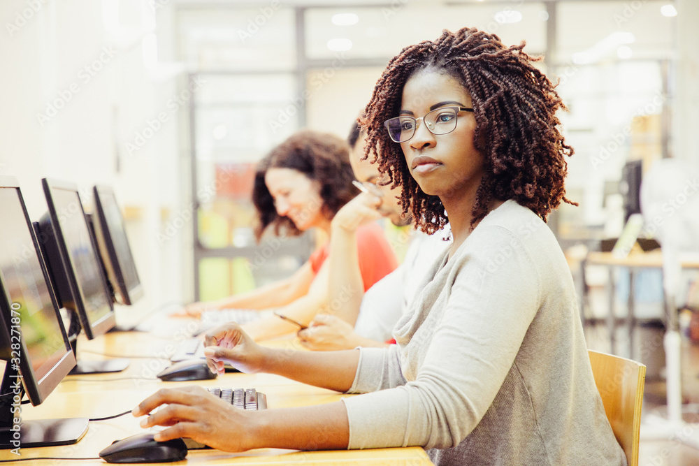 African American adult student working in computer class. Line of man and women in casual sitting at table, using desktops, typing. Staff training concept - obrazy, fototapety, plakaty 