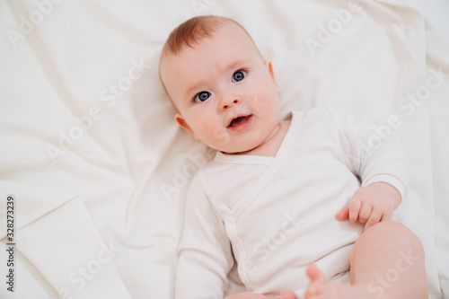 baby in white clothes lying on his back on the bed