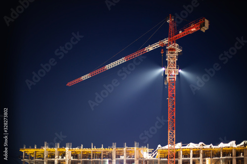 Construction crane in night illumination, construction of a multi-storey modern residential building. Night construction site, twilight spotlight