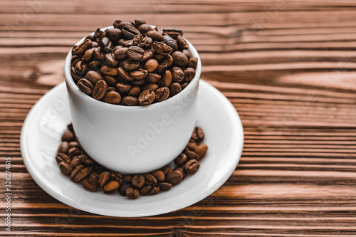full white cup with coffee beans with plate on brown wooden background