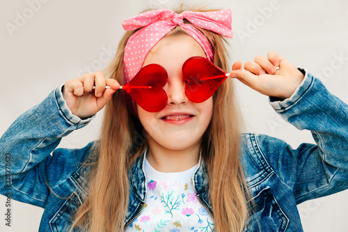 Portrait of a beautiful stylish fashionable girl in glasses, with a heart-shaped lollipop, on a white background, free time summer vacation #328278623