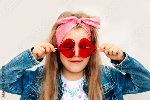 Portrait of a beautiful stylish fashionable girl in glasses, with a heart-shaped lollipop, on a white background, free time summer vacation #328278649