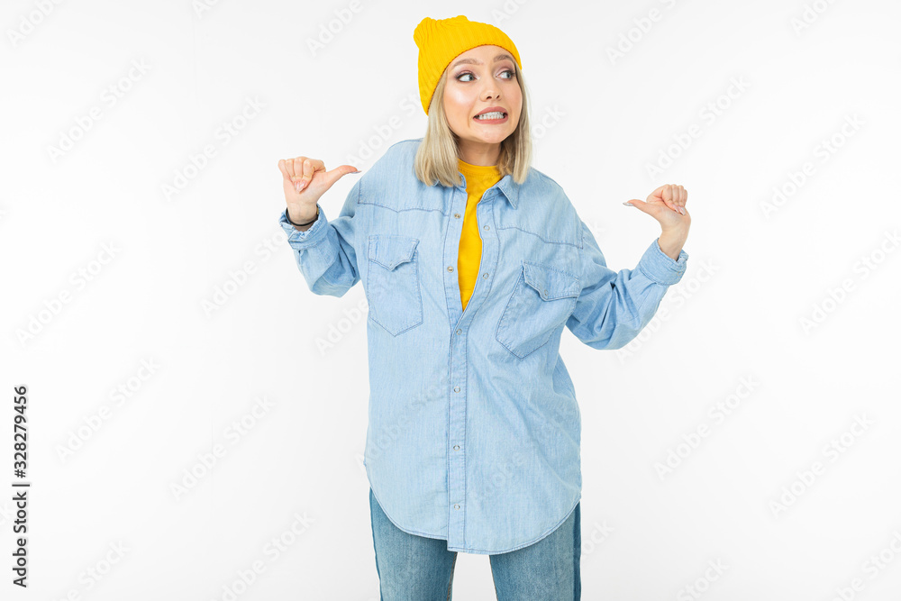 smiling cute girl in a stylish denim shirt and a yellow hat shows like on a white studio background