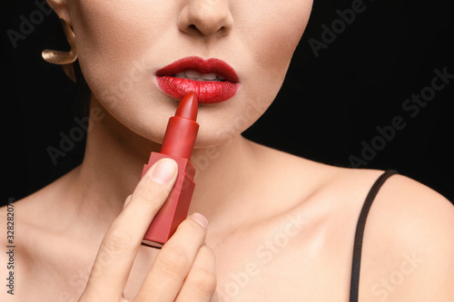 Beautiful young woman applying makeup against dark background, closeup