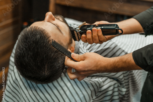 Beauty shop for men. Shaving a beard in a barbershop. Barber cuts his beard with a razor and clipper. close up Brutal haircuts. Hairdresser equipment. Selective focus. © Natalya Lys