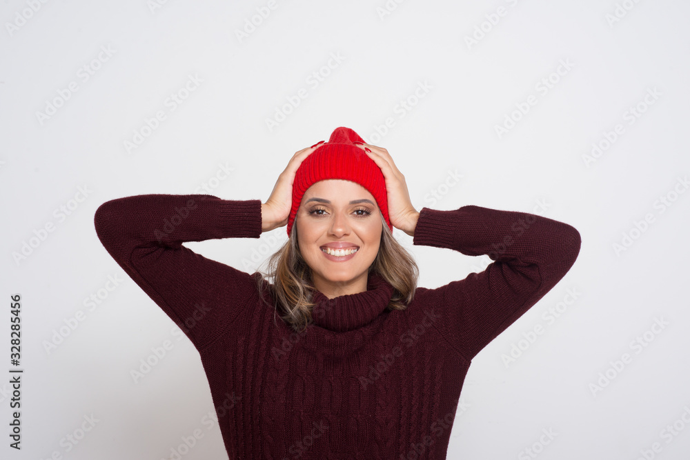 Happy young woman smiling at camera. Portrait of beautiful cheerful young blonde woman in red hat standing with hands on head and looking at camera isolated on white background. Happiness concept