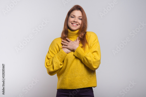 Cheerful young woman with hands on chest. Beautiful happy young woman holding hands near heart and smiling at camera. Love concept © Mangostar