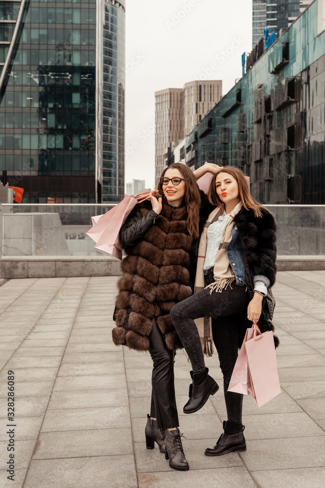 Shopping, consumption. Office center, glass buildings. Two beautiful girls are walking on the street with paper bags from shops. Shopping in the quarter of skyscrapers. Entertainment of modern women.