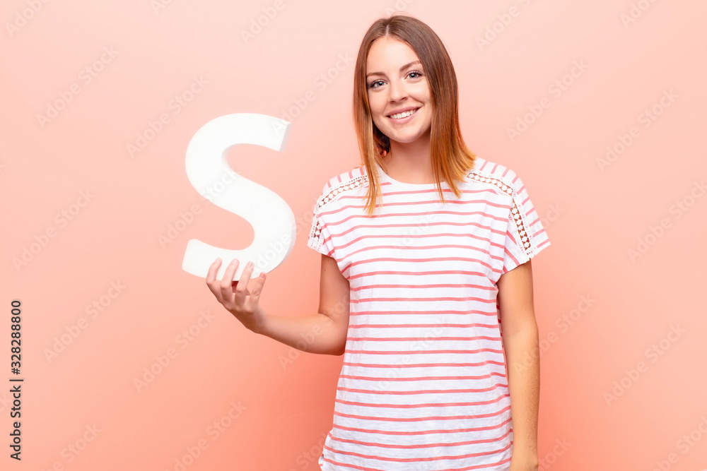 Φωτογραφία young pretty red head woman excited, happy, joyful, holding the letter S of the alphabet to form a word or a sentence