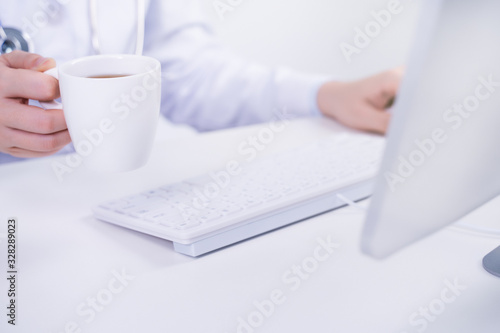 Business concept - Young female doctor woman working at office with computer, typing electronic medical record, white table background, close up, copy space