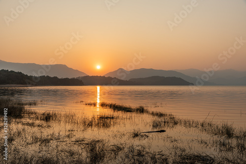 The setting sun falls in the mountains and the sun shines on the lake