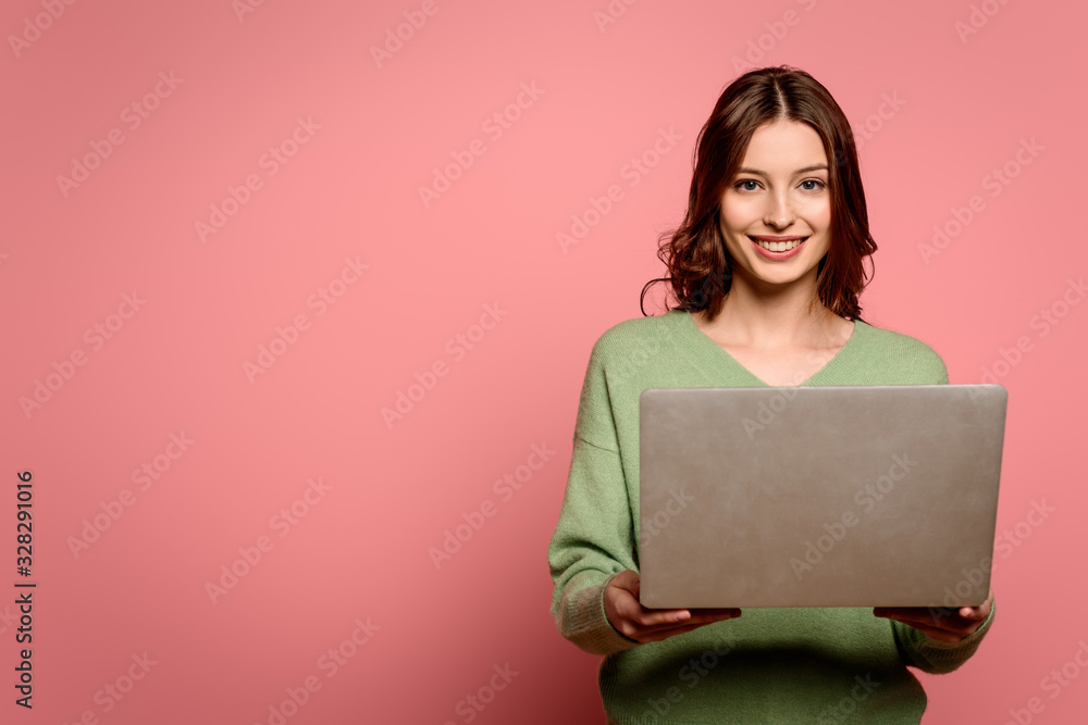 happy student holding laptop while smiling at camera on pink background happy student holding laptop while smiling at camera on pink background