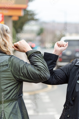 Elbow bump. New greeting to avoid the spread of coronavirus. Two women friends meet in British street with bare hands. Instead of greeting with a hug or handshake, they bump elbows instead. Vertical. photo