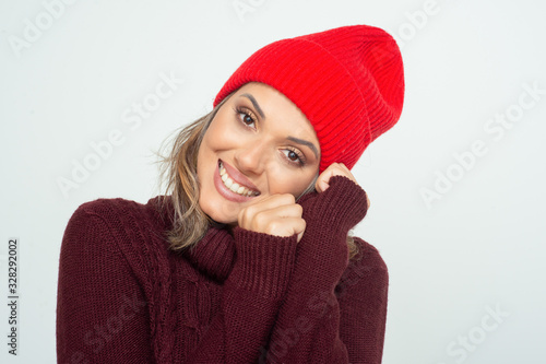 Beautiful happy woman in red hat. Portrait of beautiful young blonde woman in knitted hat and sweater posing with hands near face and smiling at camera. Beauty concept