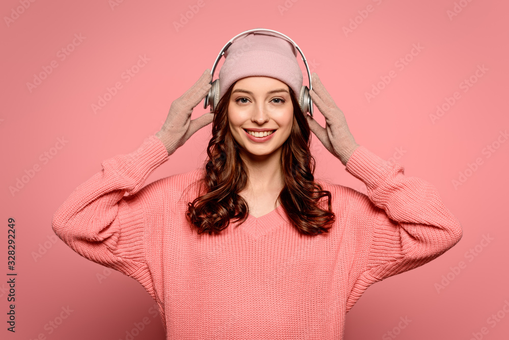 cheerful girl putting wireless headphones on while smiling at camera on pink background cheerful girl putting wireless headphones on while smiling at camera on pink background