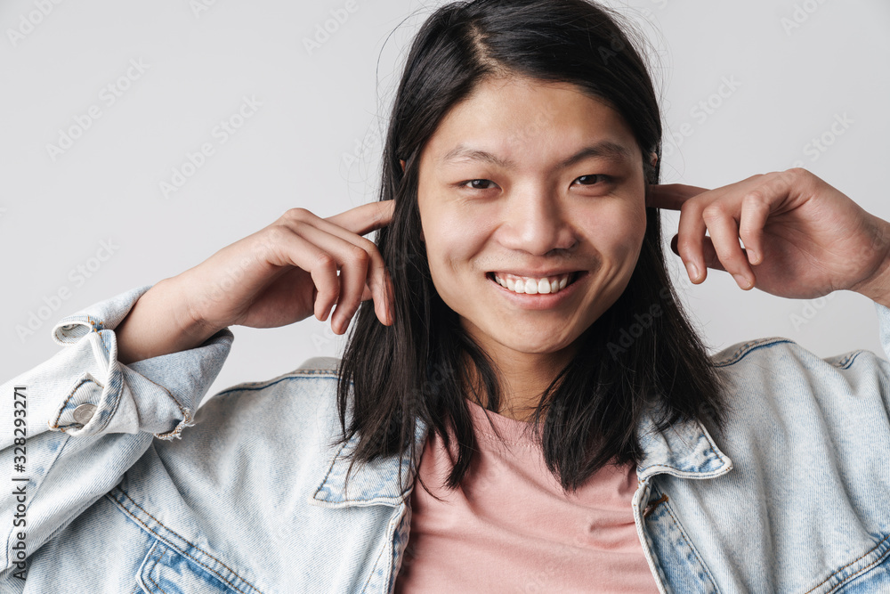 Image of pleased asian man smiling and plugging his ears Image of pleased asian man smiling and plugging his ears