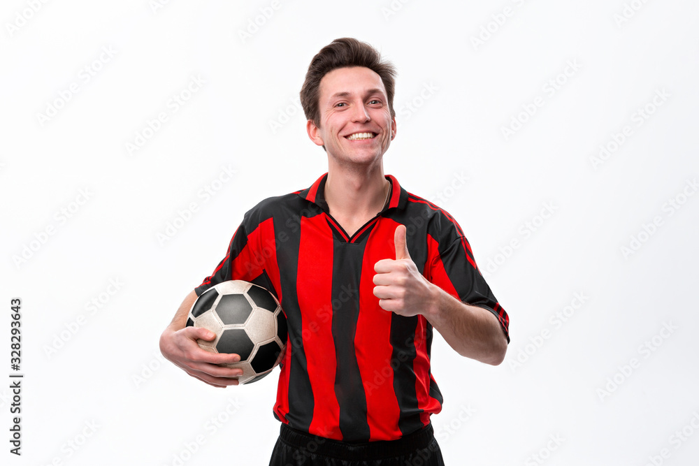 Excited soccer player in a red sportswear showing thumb up holding soccer ball.