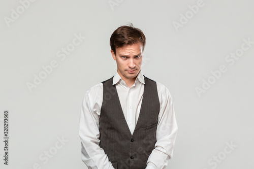 Young man in a white shirt and grey vest in high dudgeon over grey background