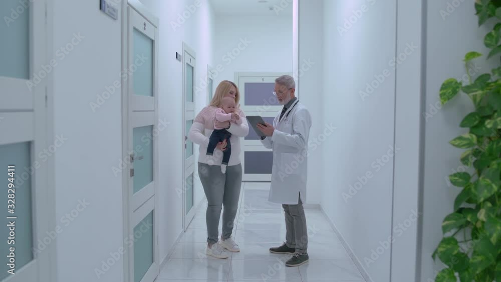 Young woman with active baby in arms talking to therapist, checking data on tab Young woman with active baby in arms talking to therapist, checking data on tab