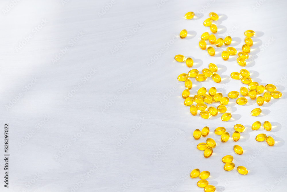 Yellow capsules with vitamin D, fish oil omega 3 with sunlight on white wooden background. Healthy and medical concept.
