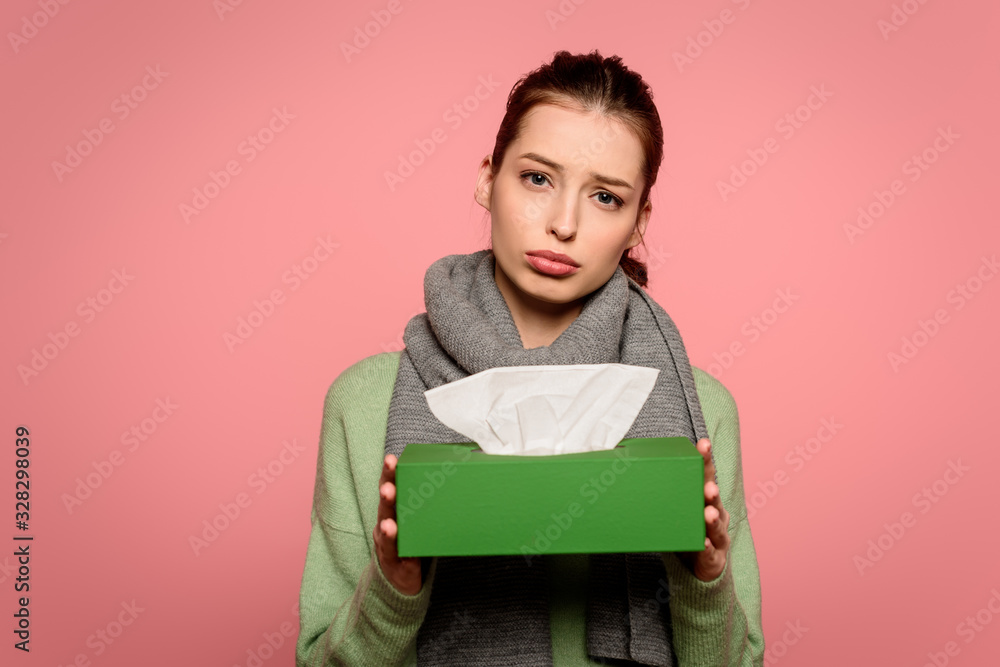 Fototapeta premium displeased, diseased girl in warm scarf taking box of paper napkins isolated on pink