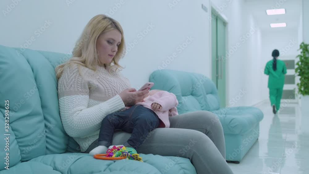 Young mother waiting doctor appointment baby sleeping in arms, clinic atmosphere Young mother waiting doctor appointment baby sleeping in arms, clinic atmosphere