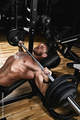 Foto Young muscular man lifting a barbell bench press in the gym