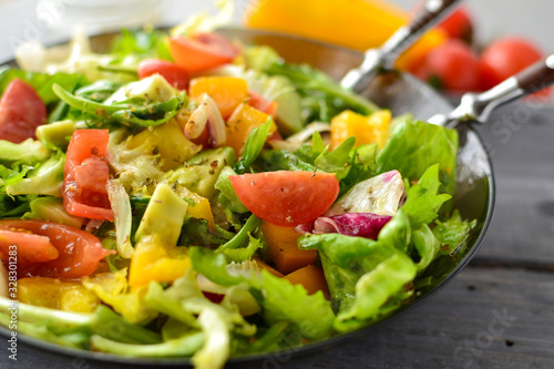 Vegan Spring Salad. Tomato, lettuce, dressing, bell peppers and avocados. Vegetable summer salad in a plate with a fork, close-up
