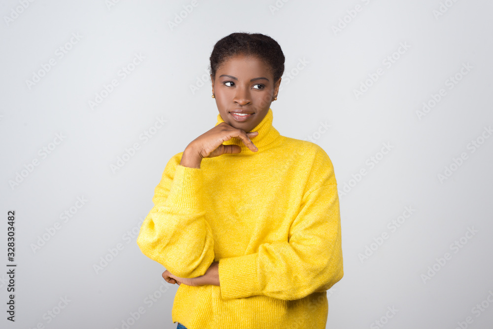 Pensive young woman looking aside. Beautiful thoughtful young African American woman standing with hand on chin and looking away. Dream concept Pensive young woman looking aside. Beautiful thoughtful young African American woman standing with hand on chin and looking away. Dream concept