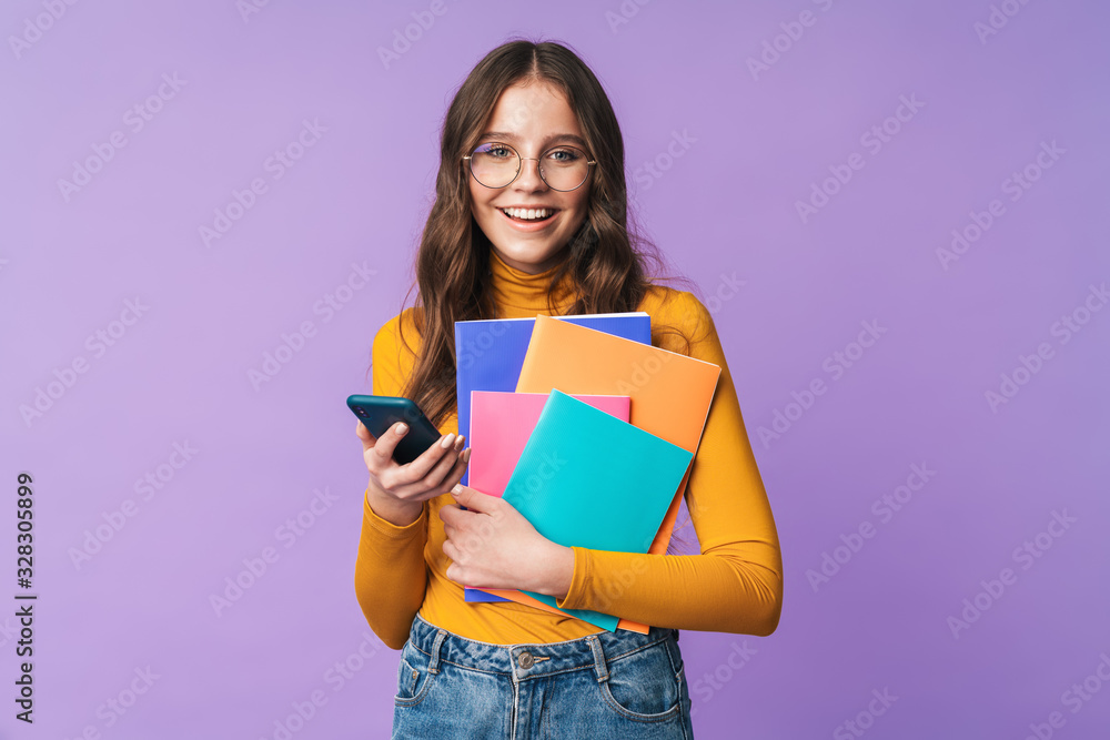 Image of young student girl holding exercise books and cellphone Image of young student girl holding exercise books and cellphone
