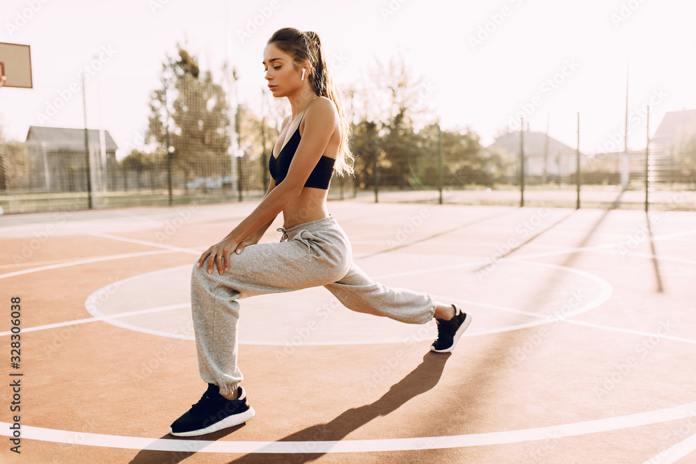 Attractive young fitness girl standing outdoors in the morning doing stretching exercises. Athletics